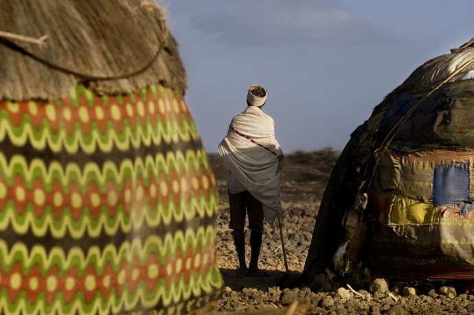 An old man stands near his hut